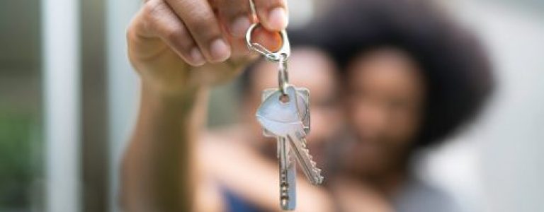 Young couple in front of a house, holding keys of their new home